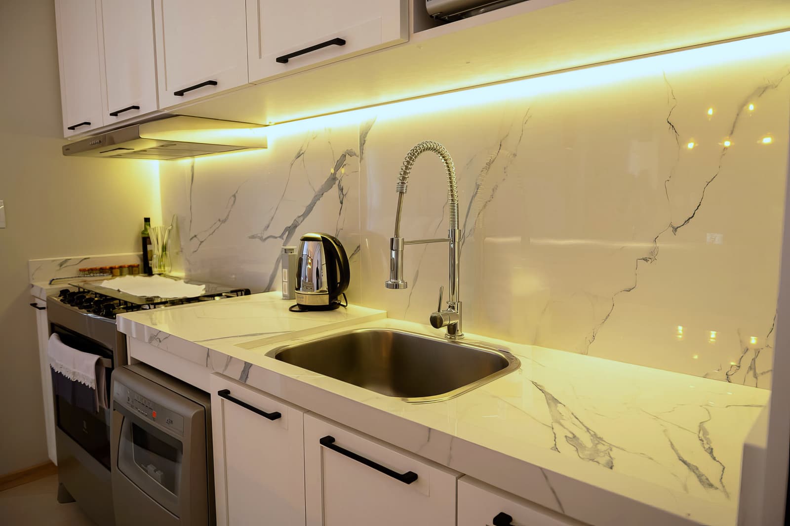 Detalhe da bancada de mármore com torneira gourmet e iluminação sob o armário