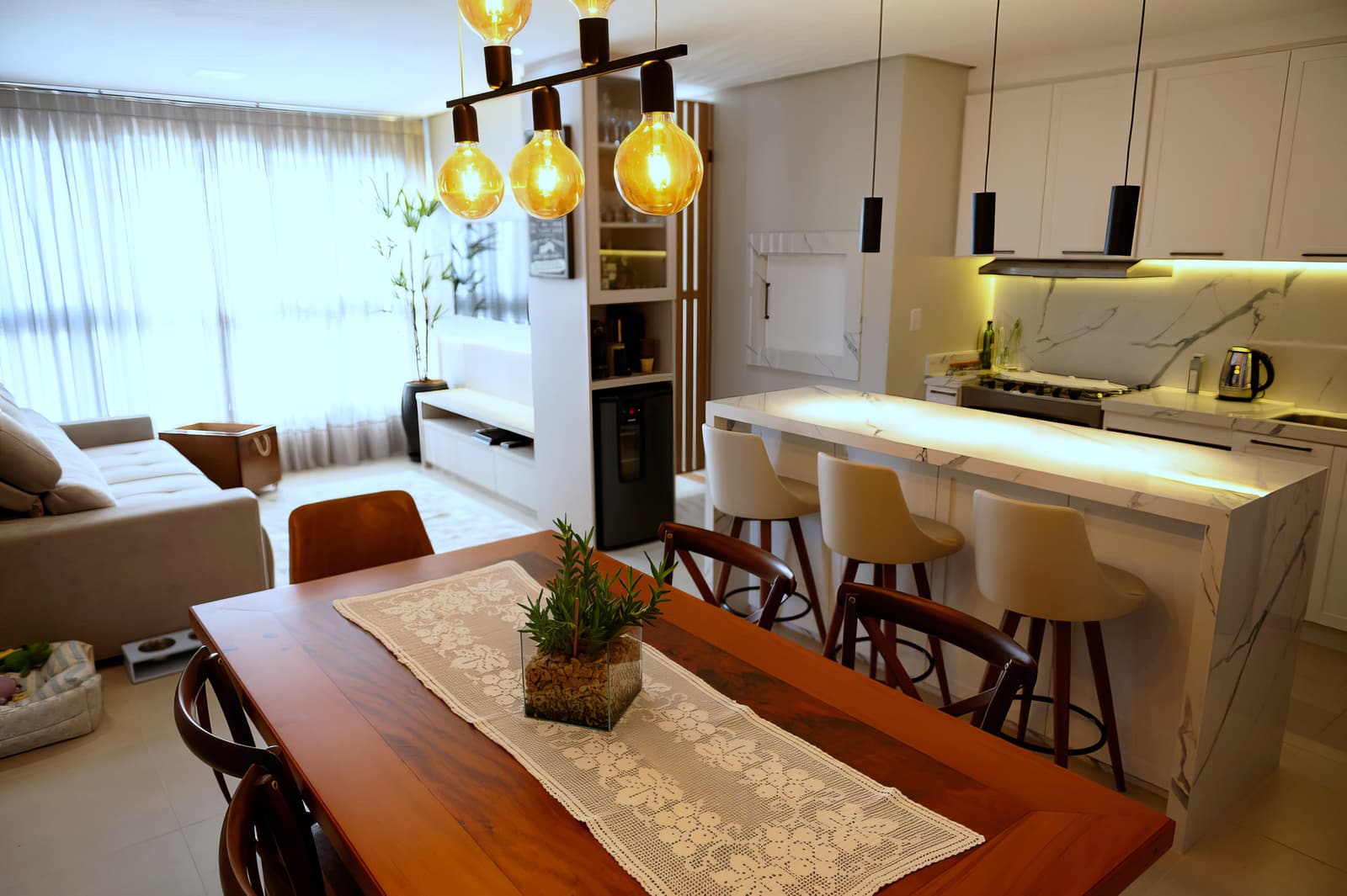Sala de estar, jantar e cozinha integradas, com pendentes de filamento e bancada de mármore