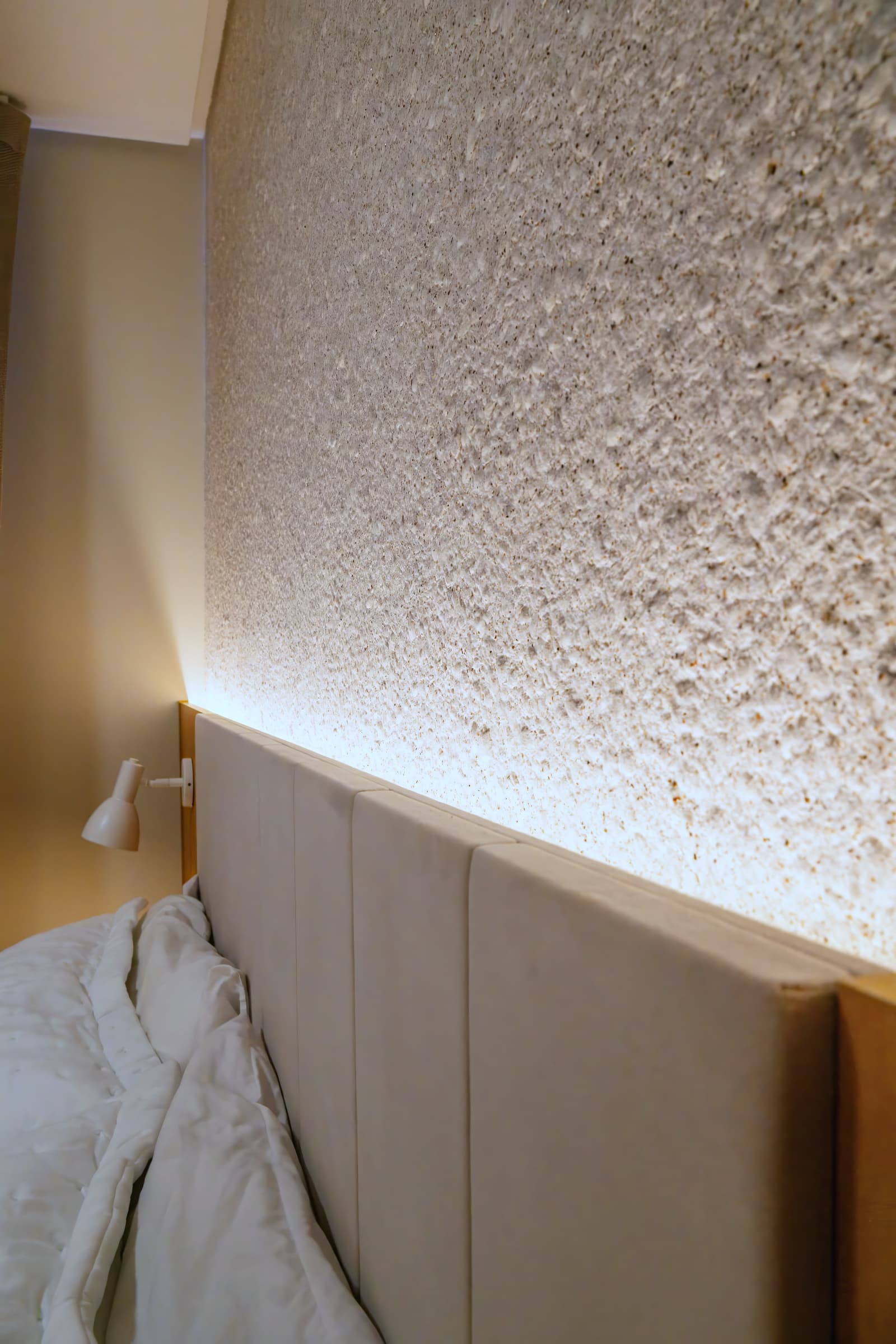 Cabeceira de parede texturizada iluminada por luz rasante