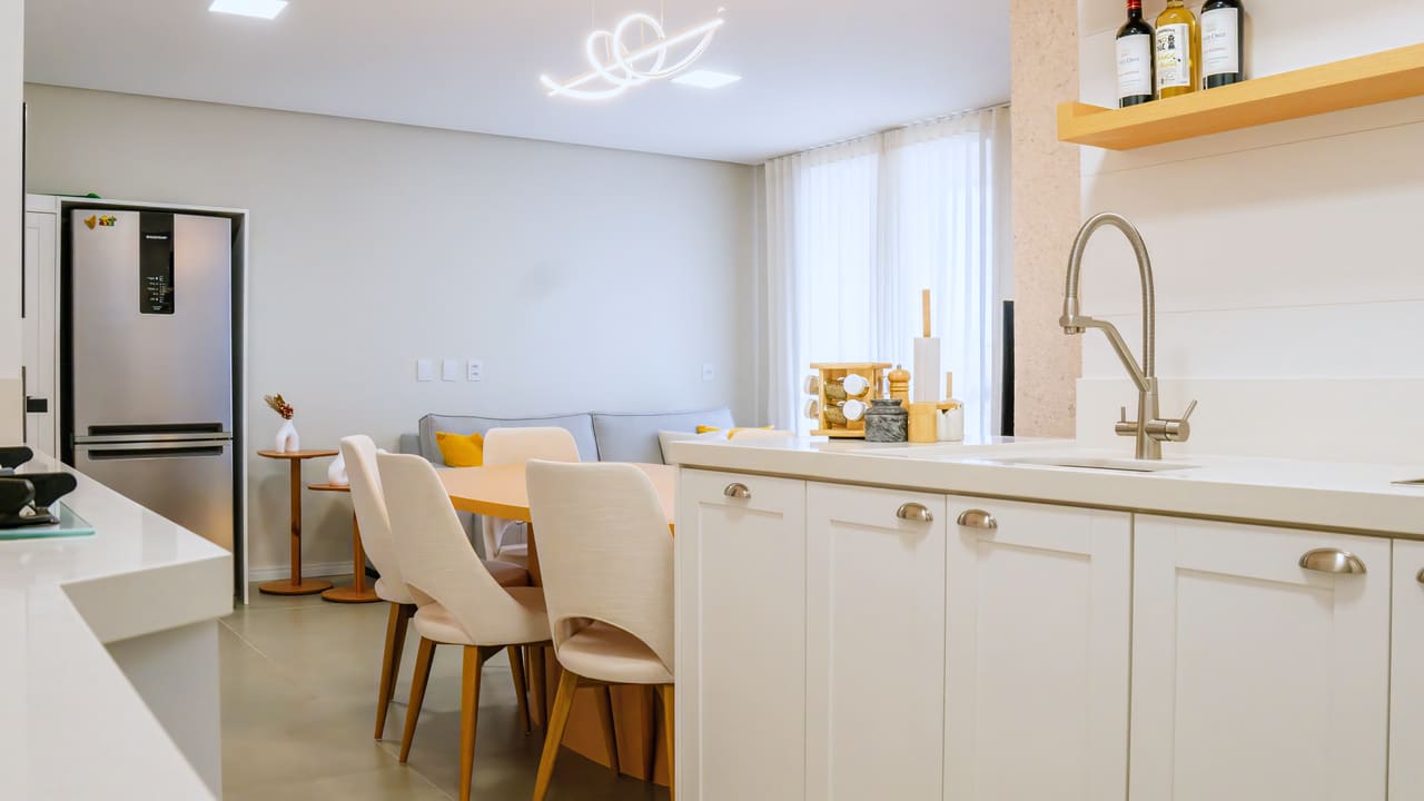 Cozinha integrada à sala de jantar, com marcenaria branca, prateleiras de madeira clara e luminária de linha contínua no teto