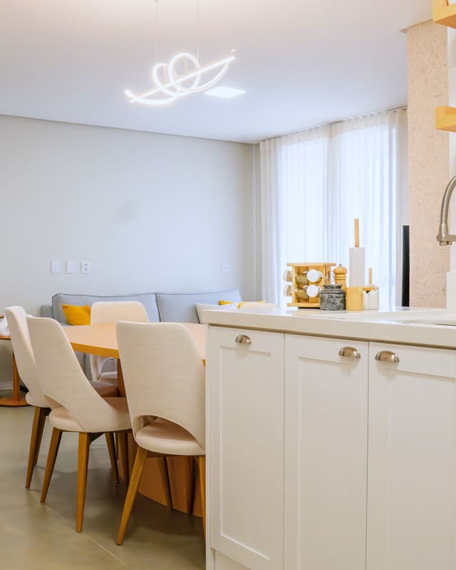 Cozinha integrada à sala de jantar, com marcenaria branca, prateleiras de madeira clara e luminária de linha contínua no teto
