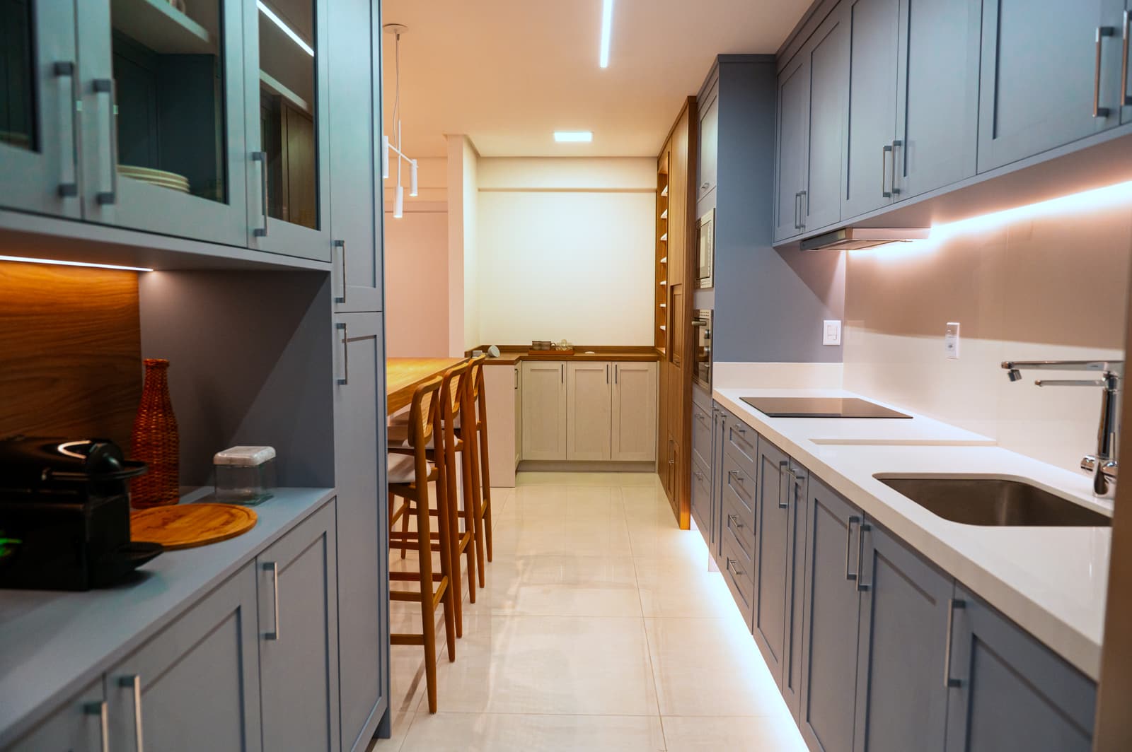 Cozinha em corredor com marcenaria azul-acinzentada e portas de vidro