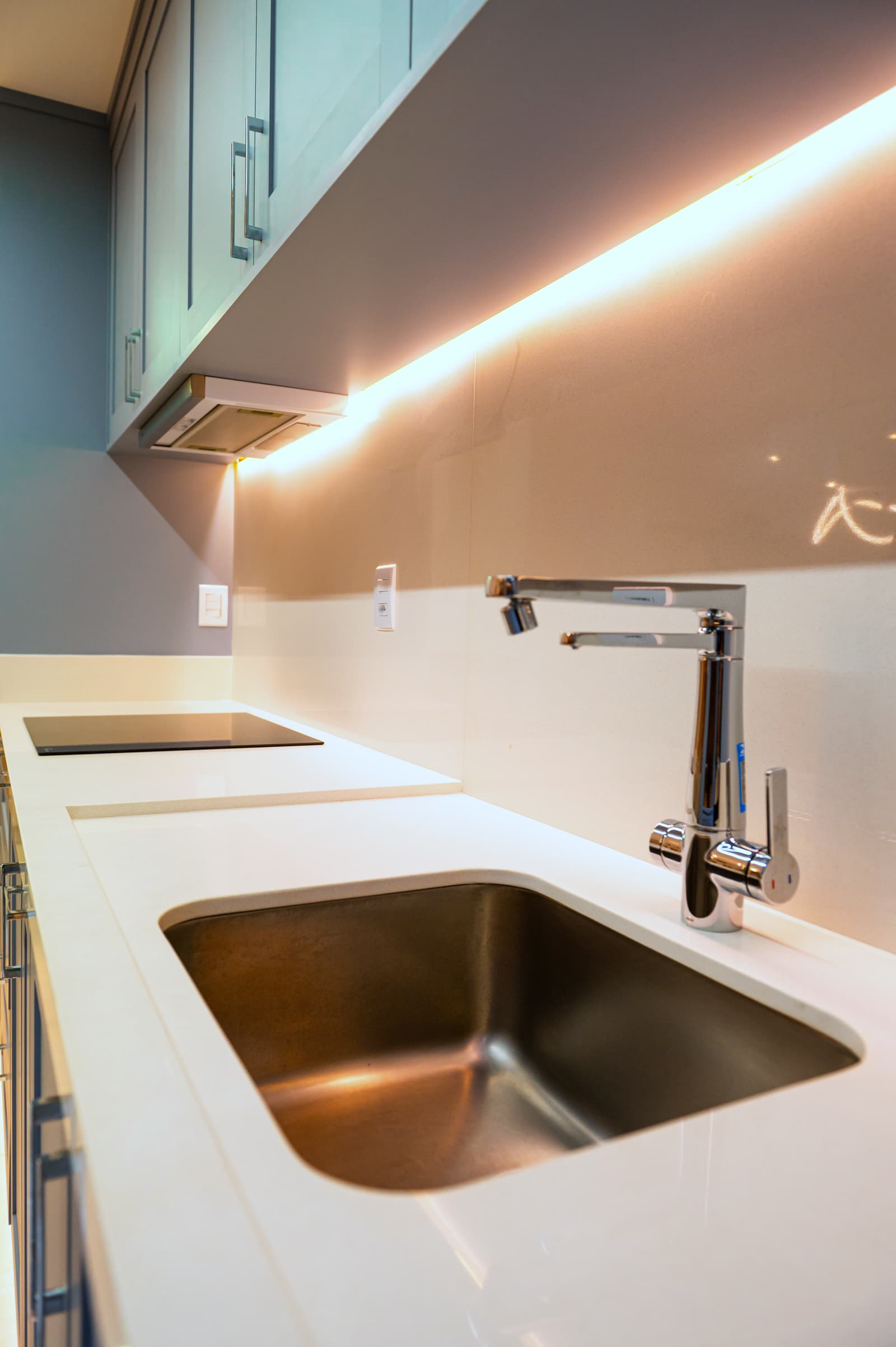 Detalhe do cooktop embutido na bancada branca, ao lado da torneira gourmet