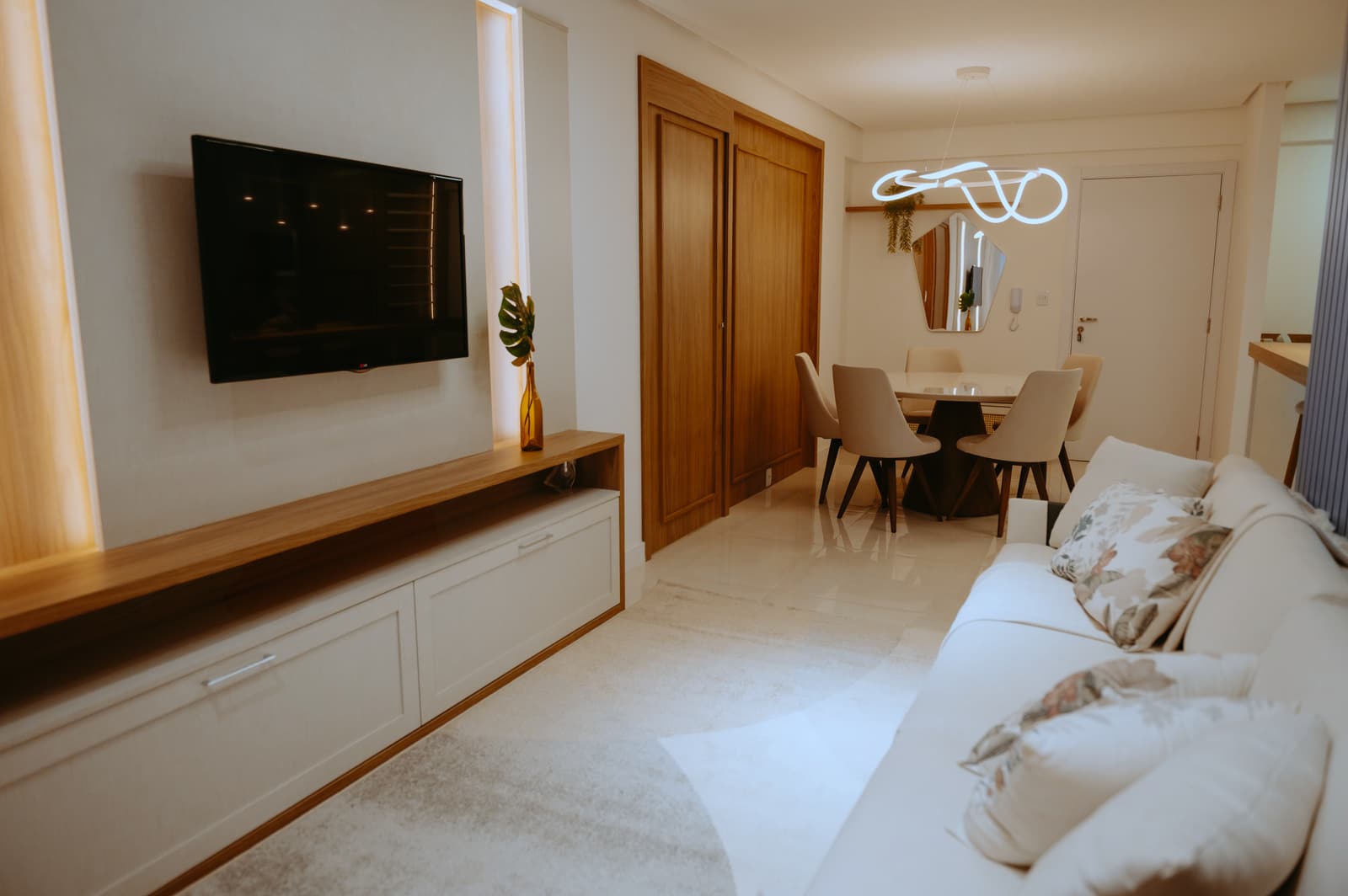 Sala de estar e jantar integradas, com mesa redonda e luminária de neon contínuo