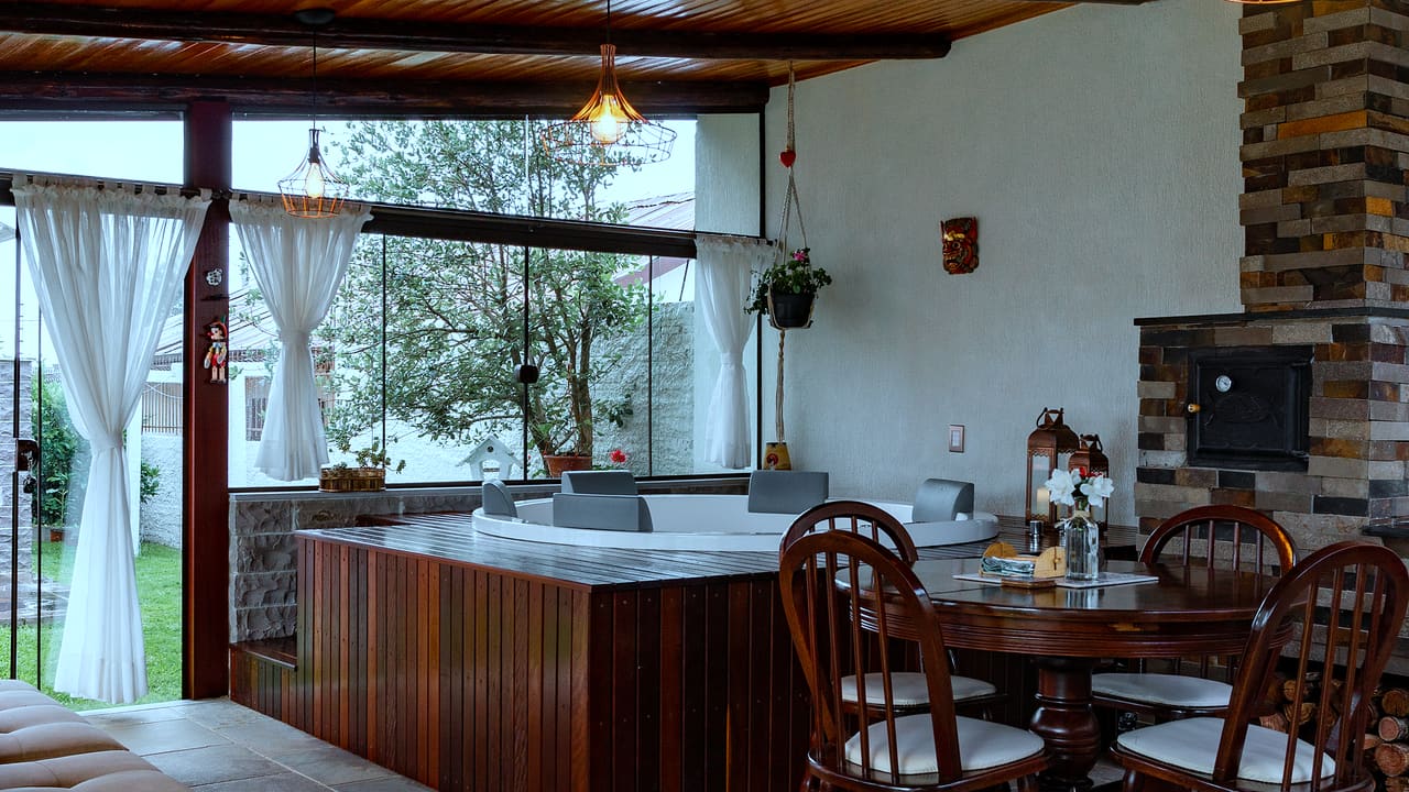 Área de lazer coberta com forro de madeira, banheira de hidromassagem e mesa de jantar junto ao jardim