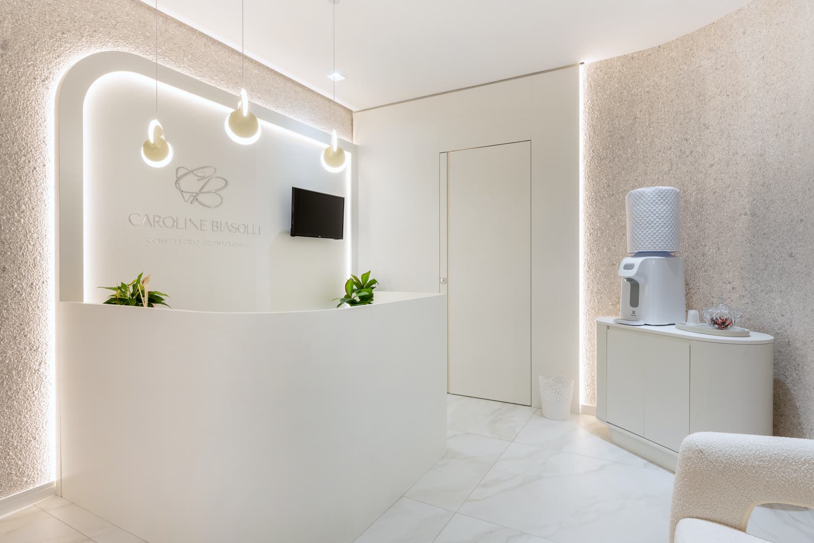 Recepção do consultório, com balcão curvo branco e iluminação linear no forro