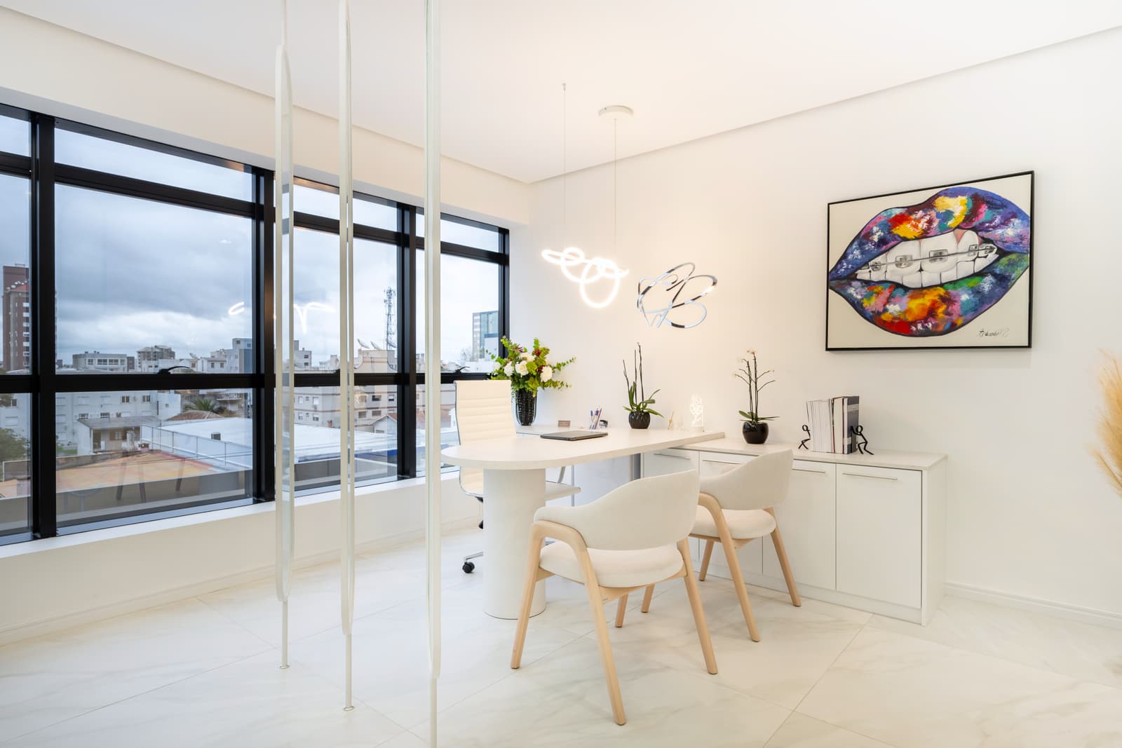 Sala de atendimento com mesa branca, cadeiras de madeira clara e vista da cidade
