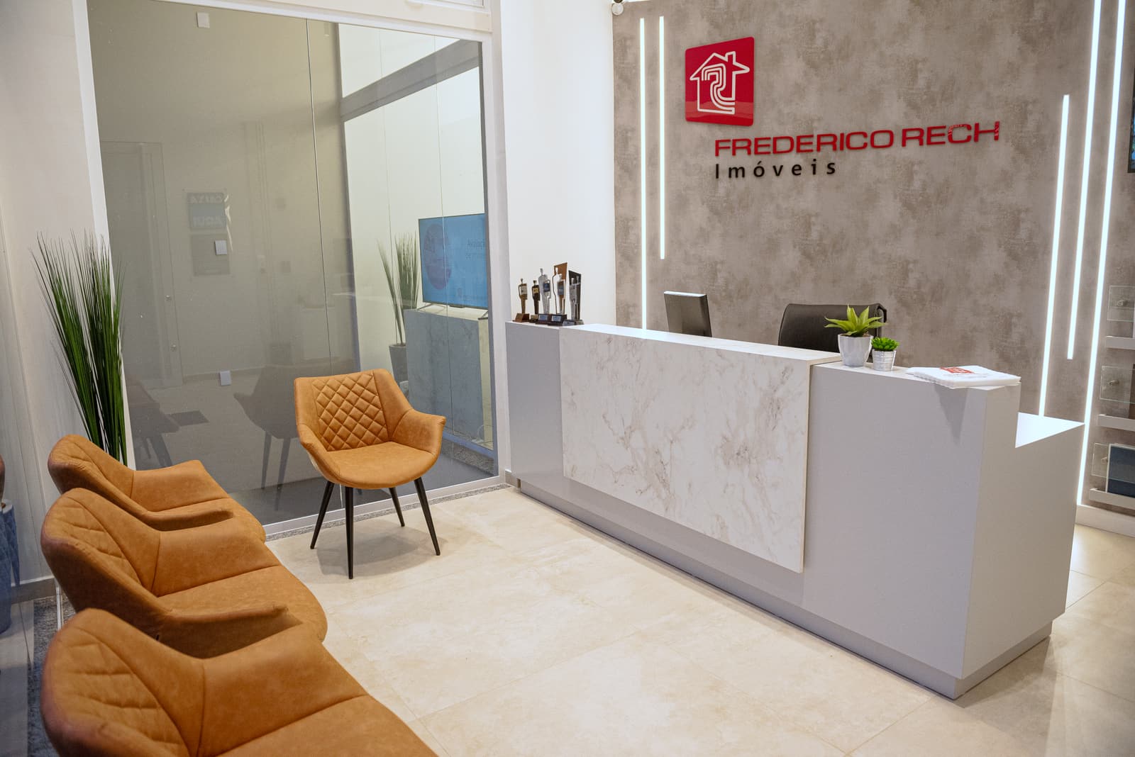 Recepção com balcão de mármore, poltronas cor de âmbar e iluminação linear