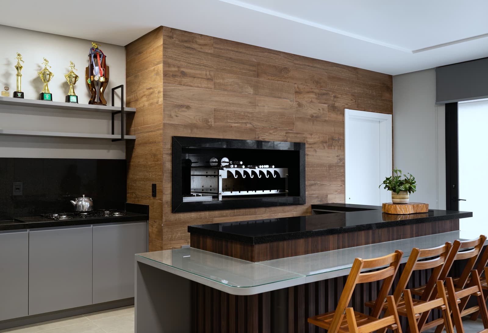 Espaço gourmet com ilha, banquetas de madeira e churrasqueira embutida em painel amadeirado