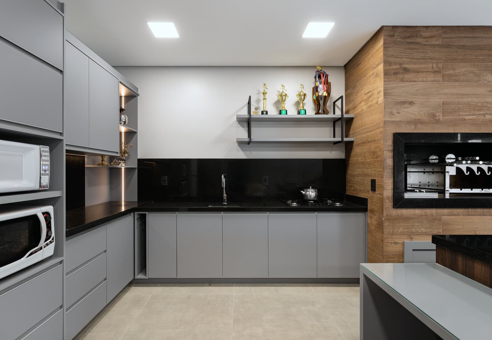 Bancada do gourmet em granito preto, com marcenaria cinza e prateleiras suspensas
