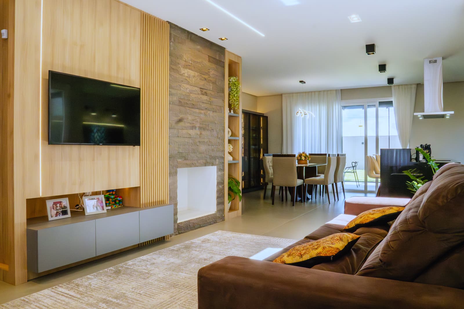 Sala de estar e jantar integradas, com painel ripado de madeira e parede de pedra