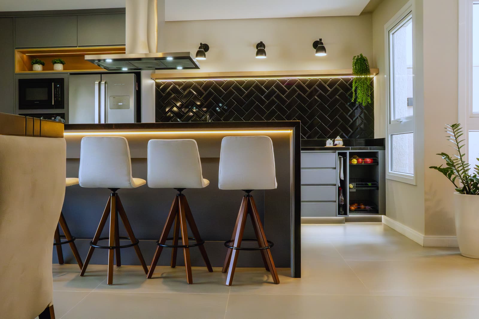 Cozinha com ilha central, banquetas de madeira e revestimento preto em espinha de peixe