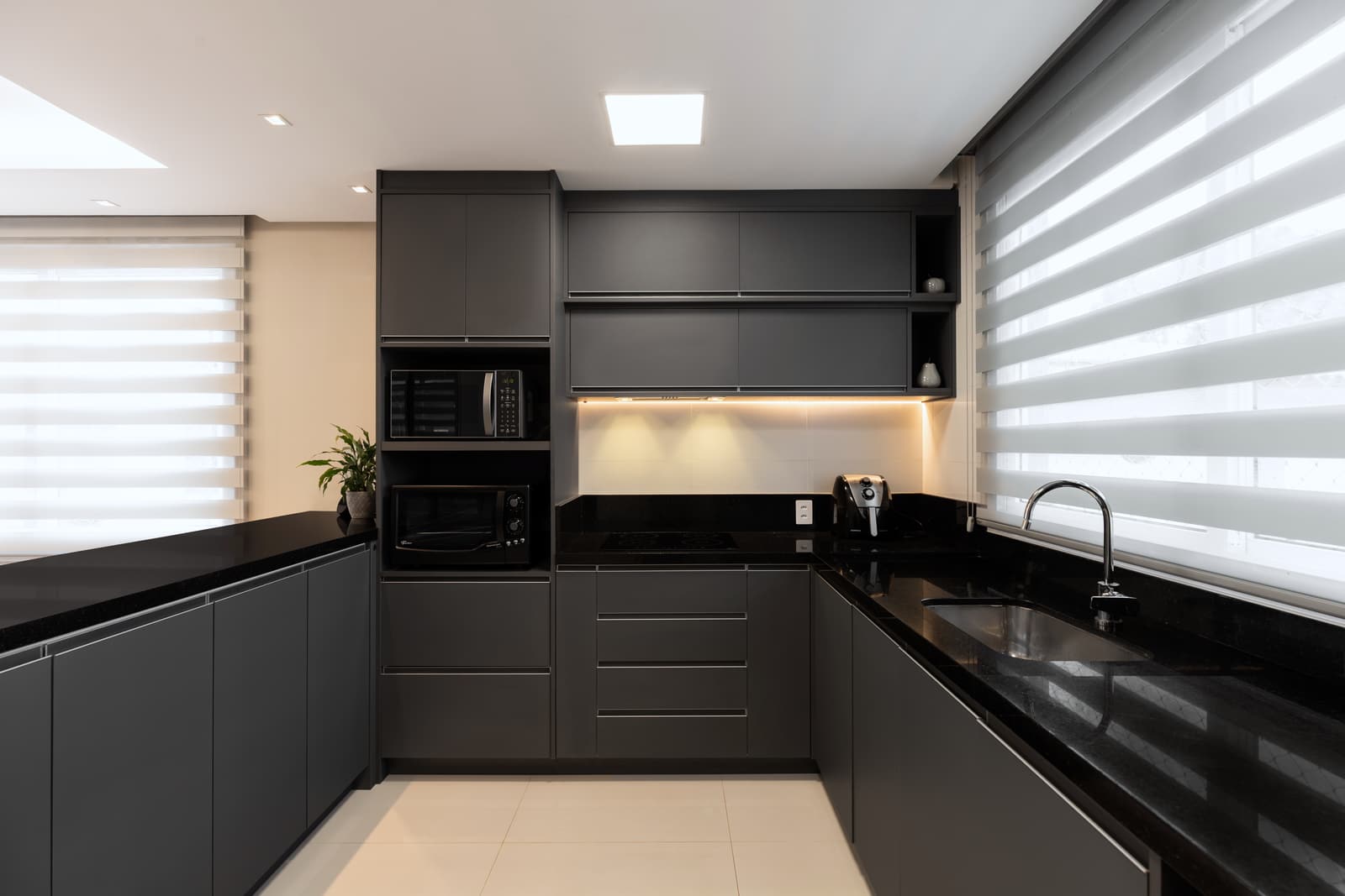 Cozinha em L com marcenaria grafite, bancada preta e iluminação linear sob os armários