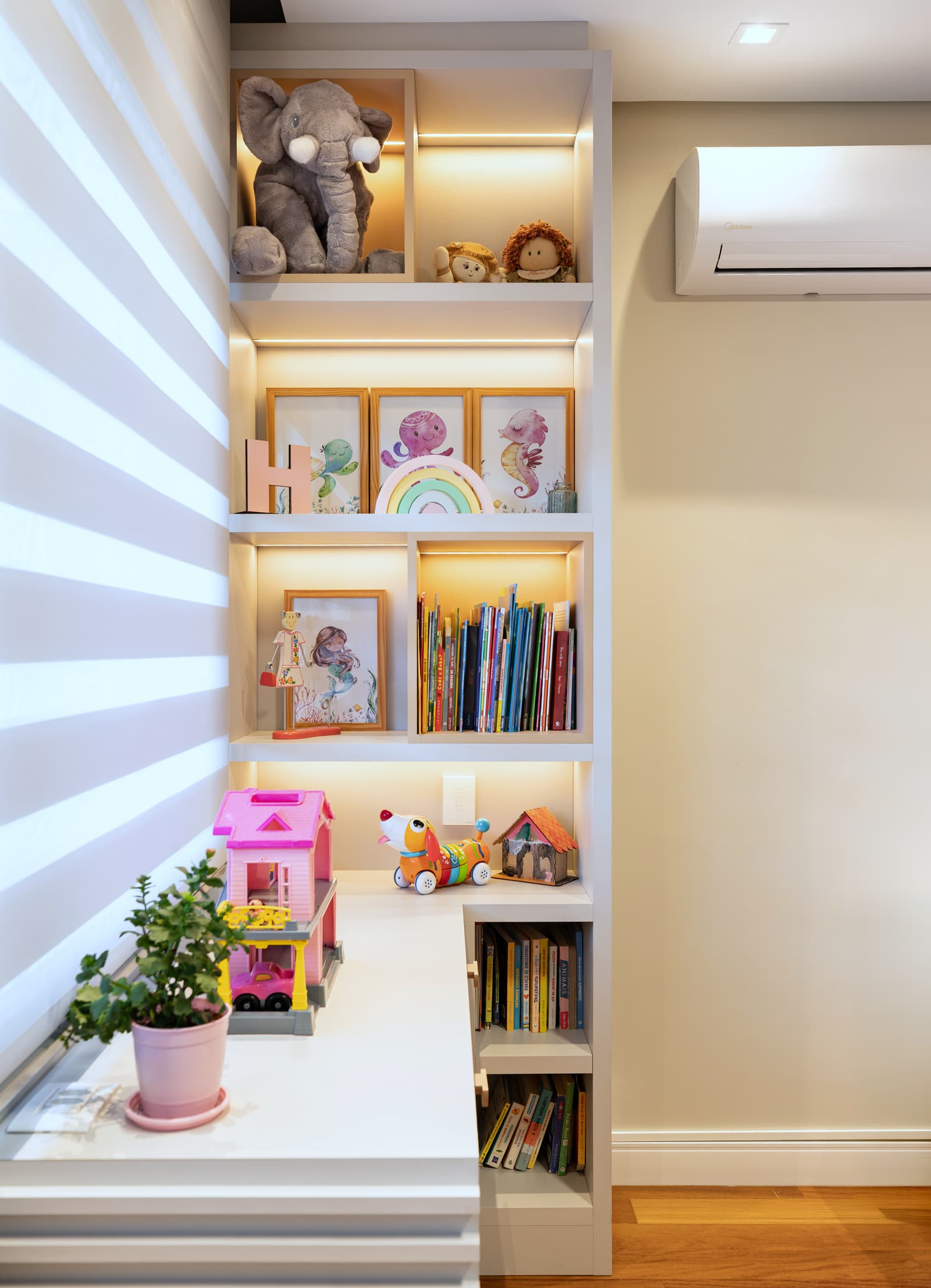 Detalhe da estante do quarto infantil, com quadros, livros e brinquedos nos nichos iluminados