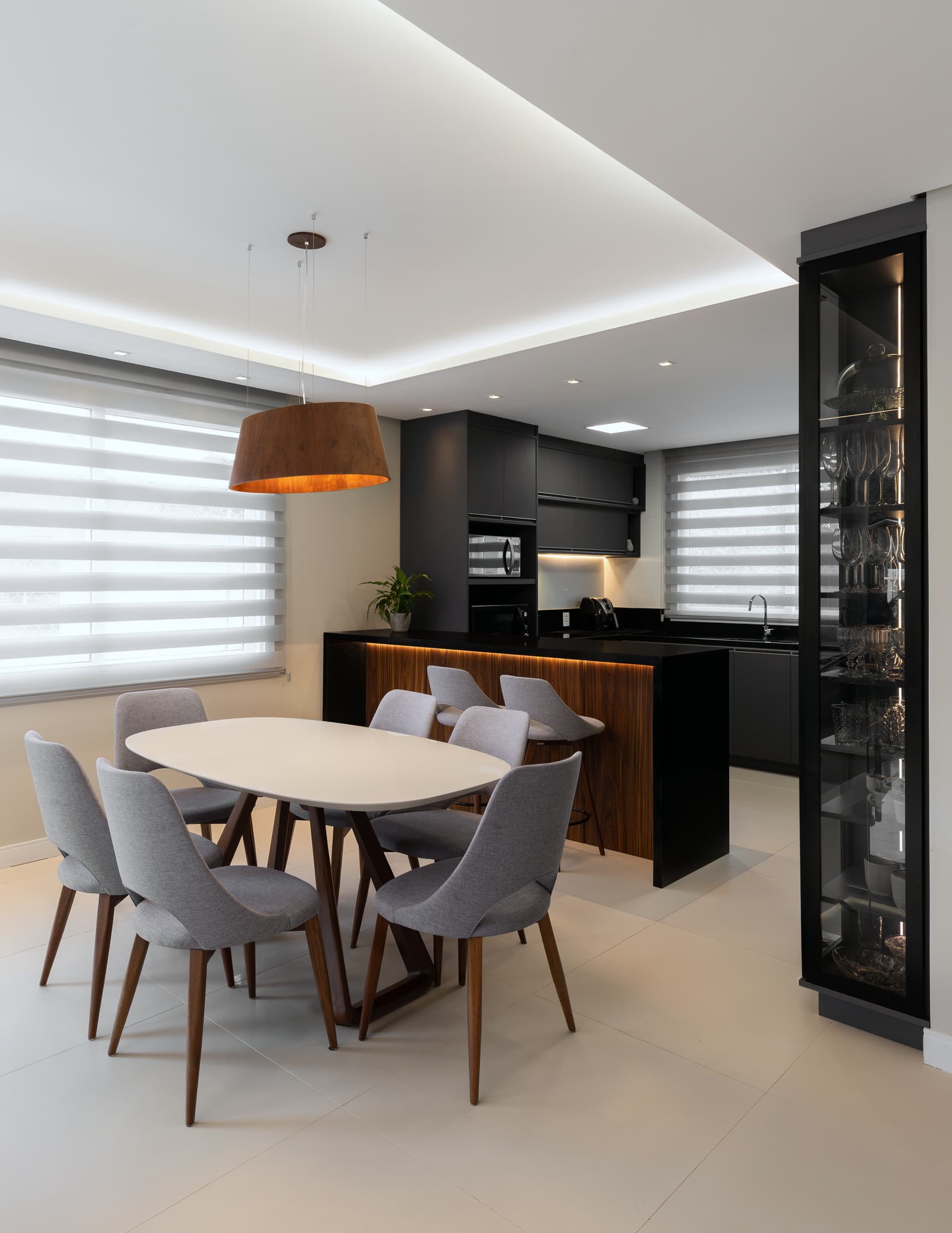 Sala de jantar com mesa redonda, pendente de cúpula e cozinha preta ao fundo