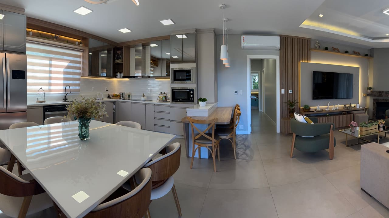 Cozinha, sala de jantar e estar integradas, com marcenaria clara, bancada branca e lareira ao fundo