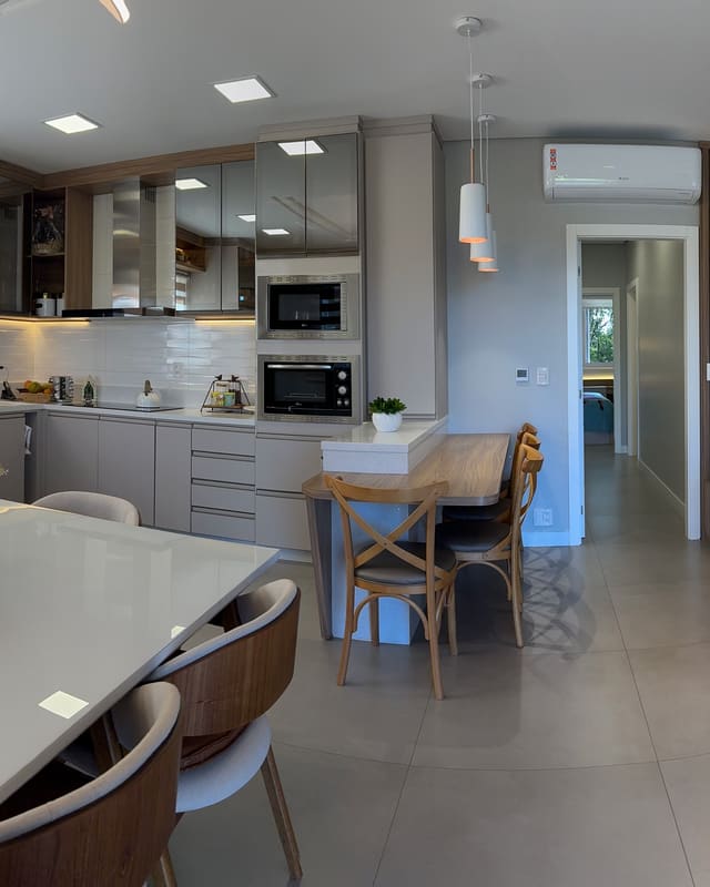Cozinha, sala de jantar e estar integradas, com marcenaria clara, bancada branca e lareira ao fundo